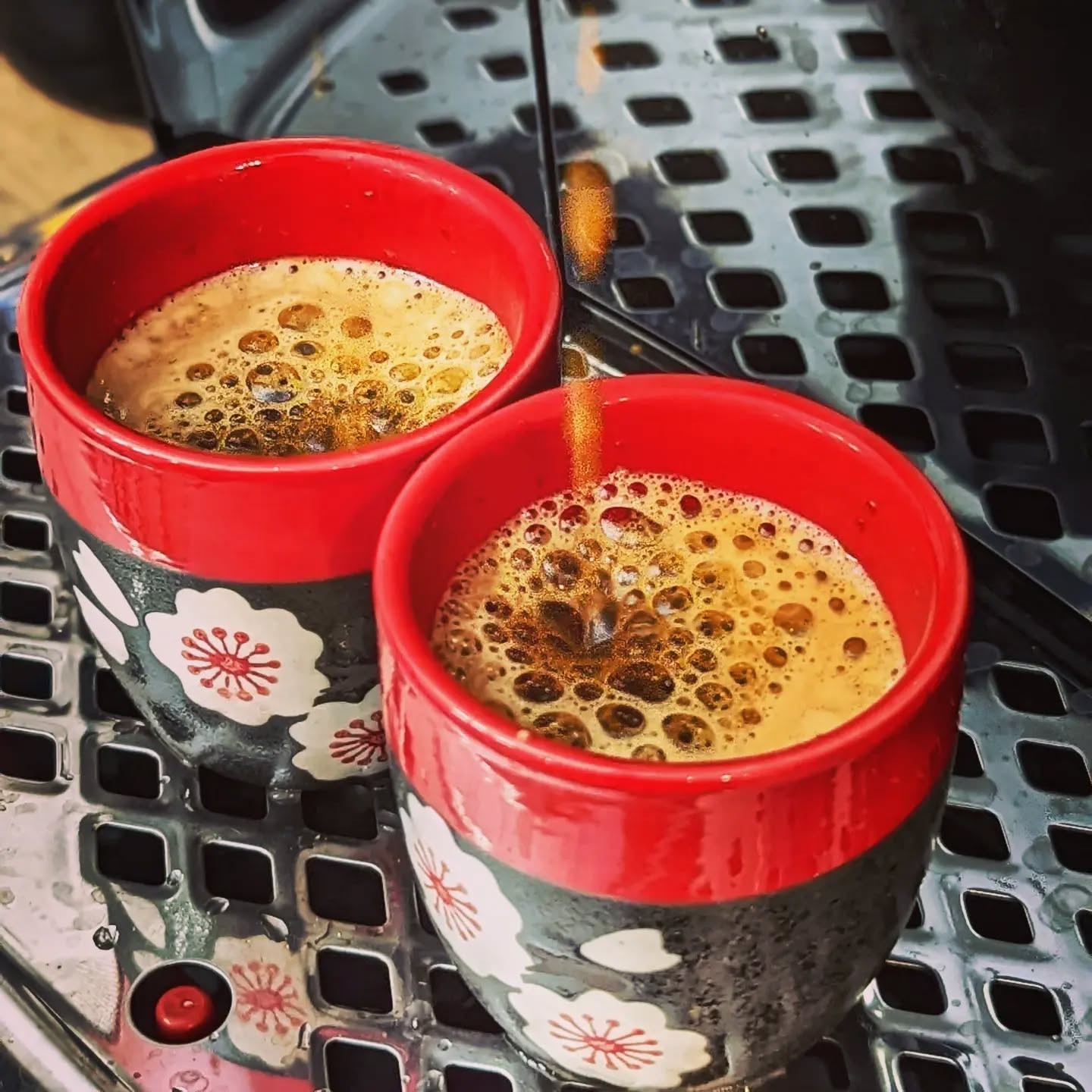 Espresso pouring into two red-and-black floral cups on the machine drip tray.