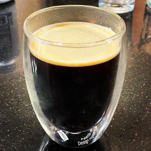 Black coffee with a golden crema layer in a clear double-wall glass.