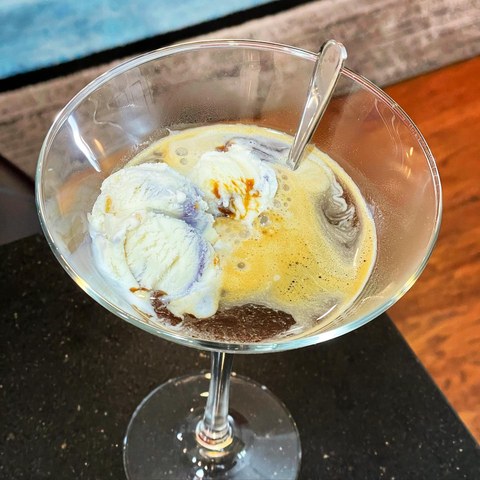 Scoops of ice cream melting into coffee in a wide stemmed glass, with a spoon.