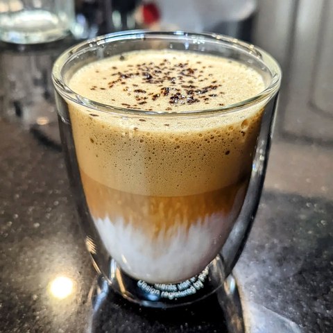 A clear glass of layered milk and whipped coffee topped with dark flecks.