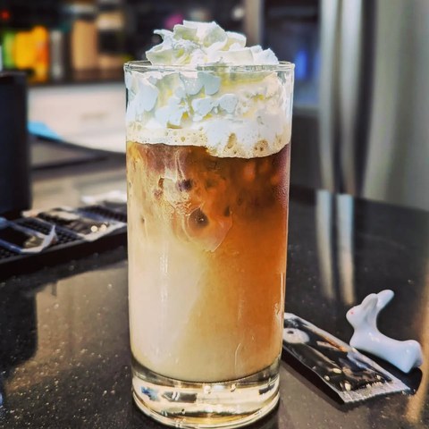 A tall glass of layered iced caramel latte topped with whipped cream on a dark counter.