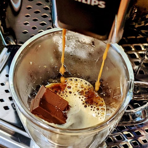 Two espresso streams falling into a glass mug containing milk and chocolate wafer pieces.