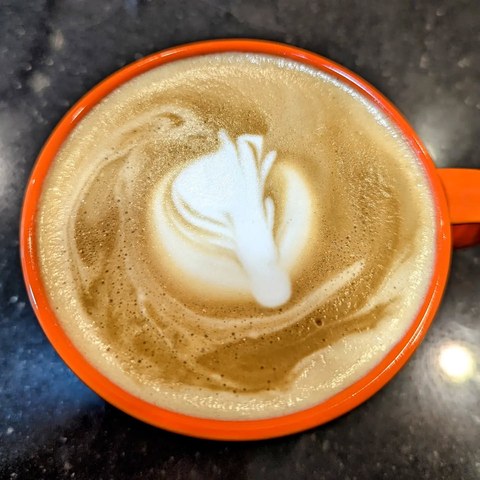 White foam art on a latte in a bright orange cup, seen from above.